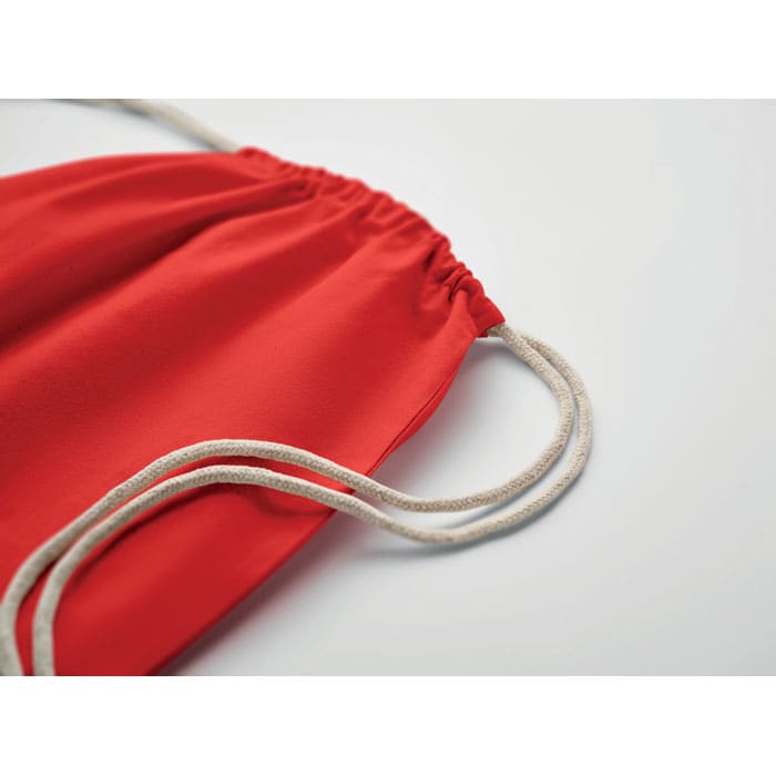 A red drawstring bag with beige cords, showcasing a smooth fabric texture and gathered top.