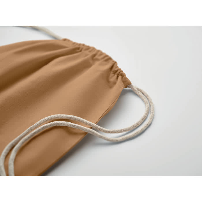 A drawstring bag in a warm tan colour with cream-coloured cords. It has a simple, minimal design.