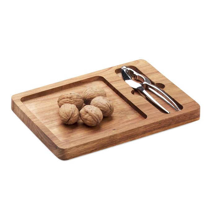 A wooden nutboard with walnuts and a silver nutcracker, featuring a cut-out section for easy cracking.