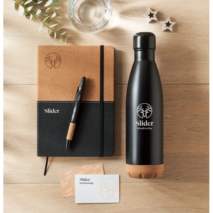 A drink bottle in black and brown, alongside a notebook, pen, and business card on a wooden surface.