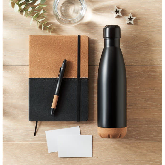 A drink bottle in matte black with a brown base, alongside a notebook, pen, and blank cards on a wooden surface.