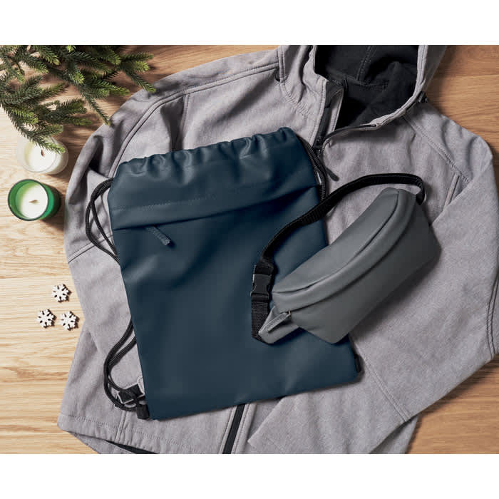 A navy drawstring bag, a grey pouch, and a grey hoodie are arranged on a wooden surface with decorative elements.