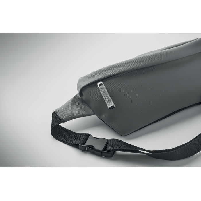 A grey waist bag with a zippered pocket and an adjustable black strap, featuring a logo on the zipper.