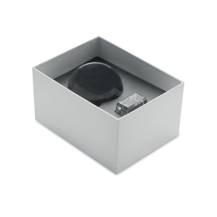 A boxed set with a black dome-shaped item and a clear rectangular piece, both resting on a grey background.