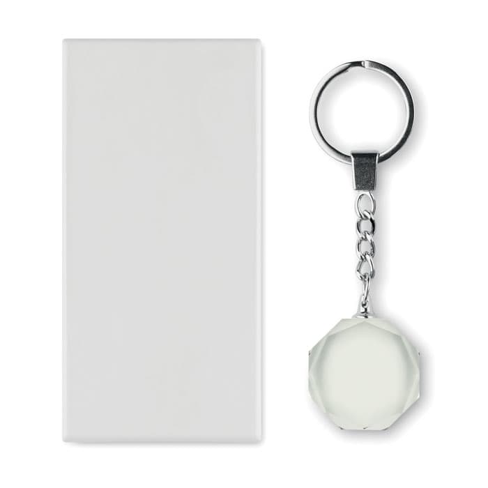 A keyring with a faceted clear pendant next to a plain rectangular white surface. The keyring has a metal attachment.