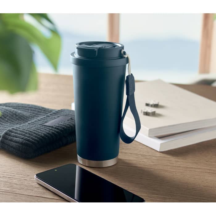 A drink bottle with a navy blue exterior and silver base, accompanied by a beanie and smartphone on a wooden table.