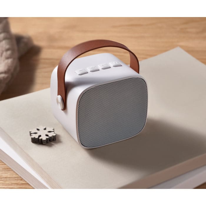 A compact white speaker with a brown handle, placed on a light-coloured surface beside a decorative item.