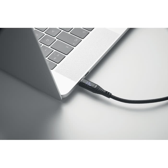 A close-up of a laptop with a black cable connected to one of its ports. The laptop features a silver finish.