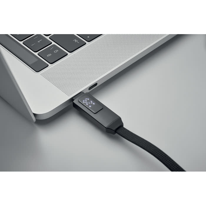 A USB drive with a textured black casing connected to a laptop. The device has a logo on it.