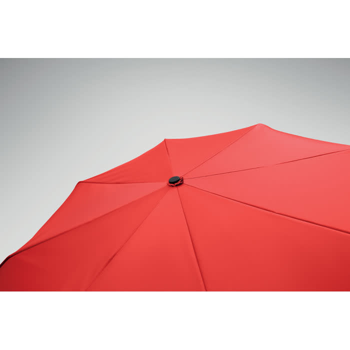 A red umbrella with a central button featuring multiple ribs for support. The background is minimal and neutral.