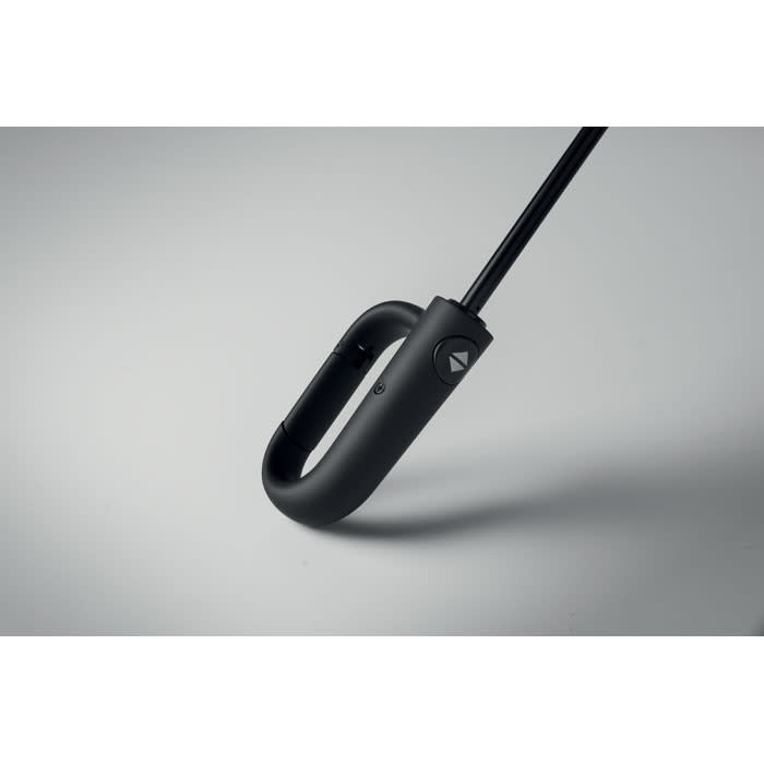 A black umbrella with a hook handle and a logo, resting on a light grey surface.