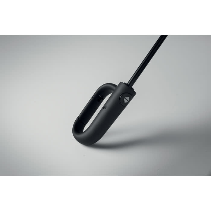A black umbrella handle with a curved hook and a button, resting on a grey surface. It features a logo on the handle.