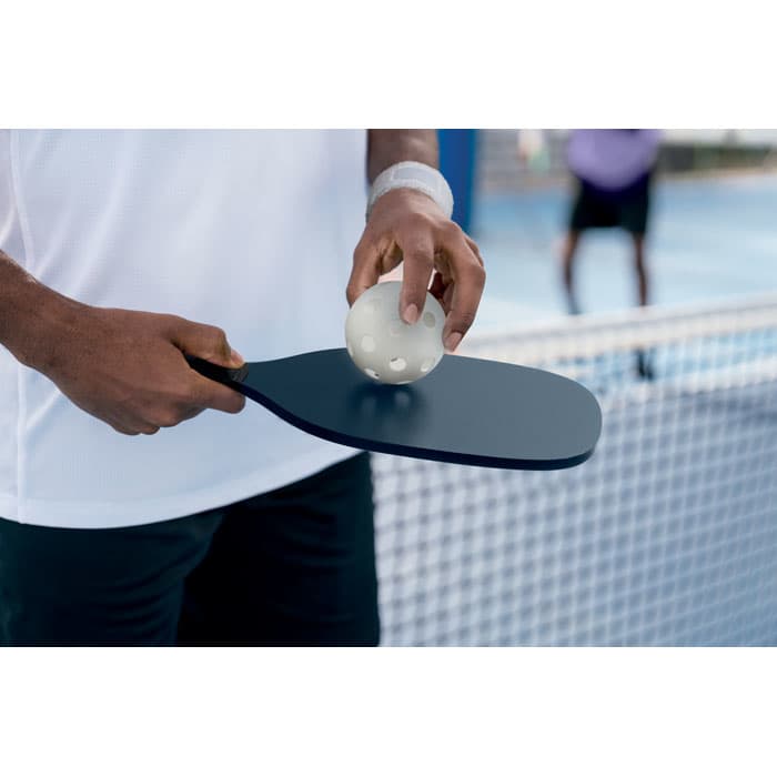 A paddle in hand, featuring a blue surface, with a white ball resting on it near a net.