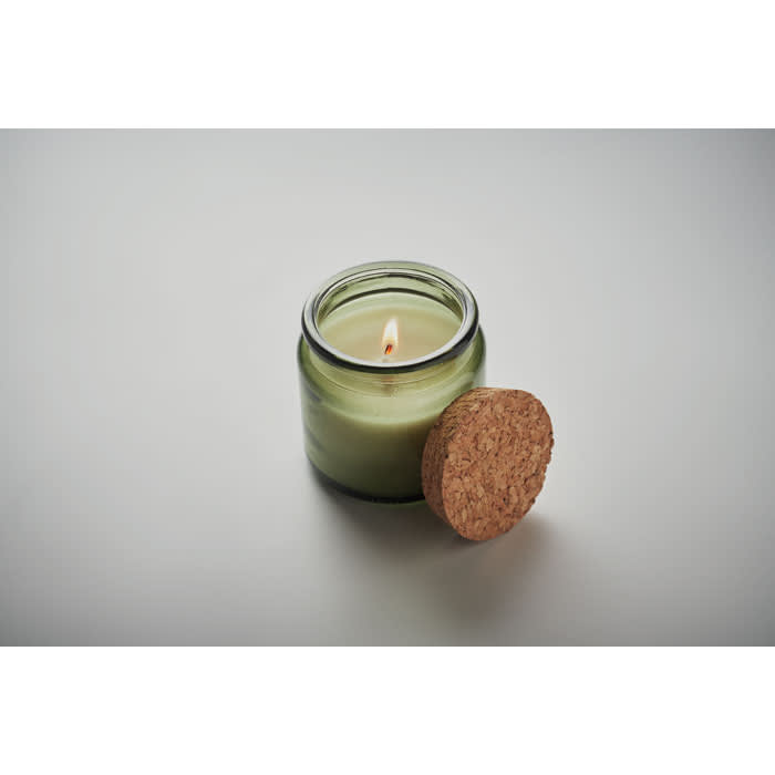 A green candle in a glass jar with a cork lid, featuring a small flame.