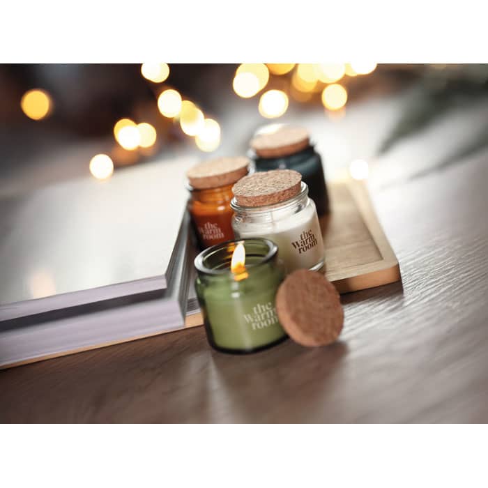 A set of four scented candles in glass jars with cork lids, featuring green, orange, white, and dark green colours.