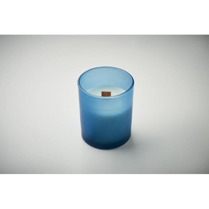 A blue frosted candle with a wooden wick, presented in a cylindrical glass holder.