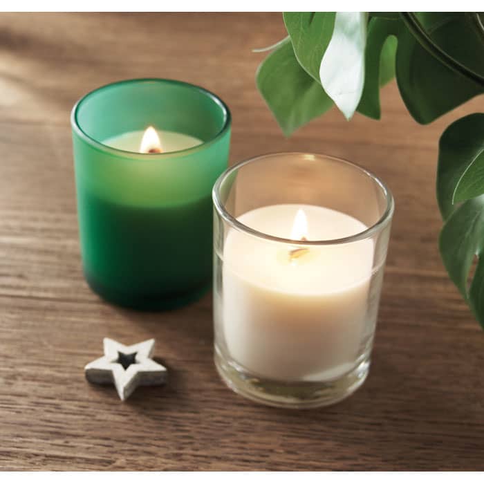 Two candles sit on a wooden surface: one green frosted glass and one clear glass with a white candle, alongside a star-shaped decoration.