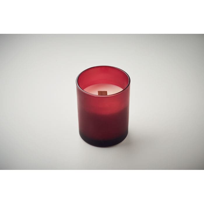 A red candle in a glass holder with a wooden wick, set against a neutral background.