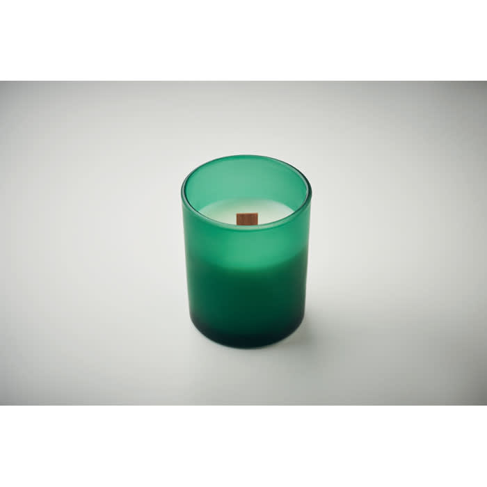 A green candle in a frosted glass holder with a wooden wick, set against a light background.