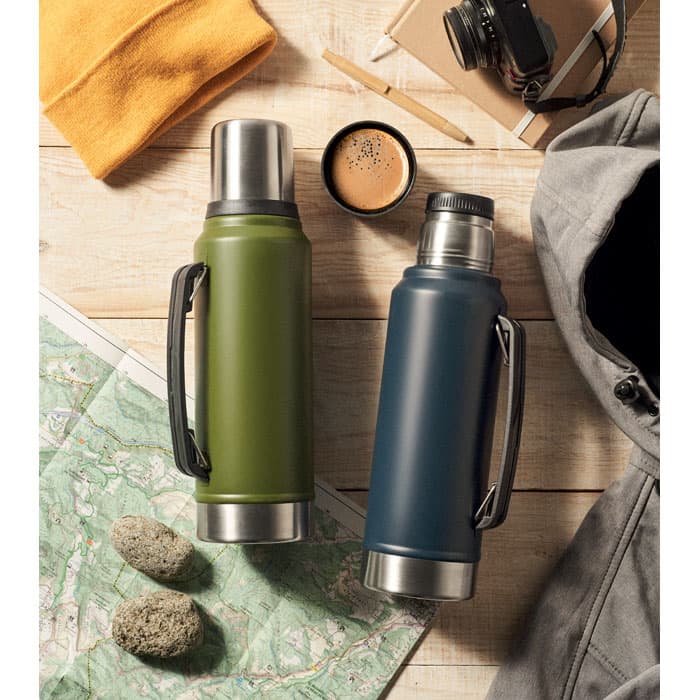 A drink bottle in olive green and a navy blue with stainless steel accents, alongside outdoor gear on a map.