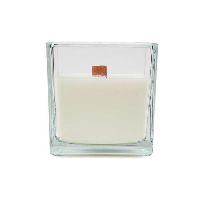 A glass candle holder containing a white wax candle with a wooden wick inside.