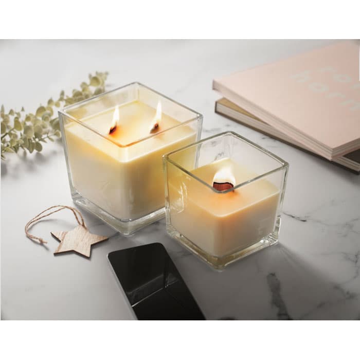 Two square glass candles with lit wicks, placed on a marble surface beside books and decorative items.