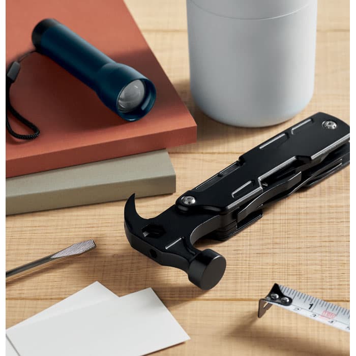 A multifunctional tool featuring a hammer, screwdriver, and ruler, set beside a torch and various coloured books.