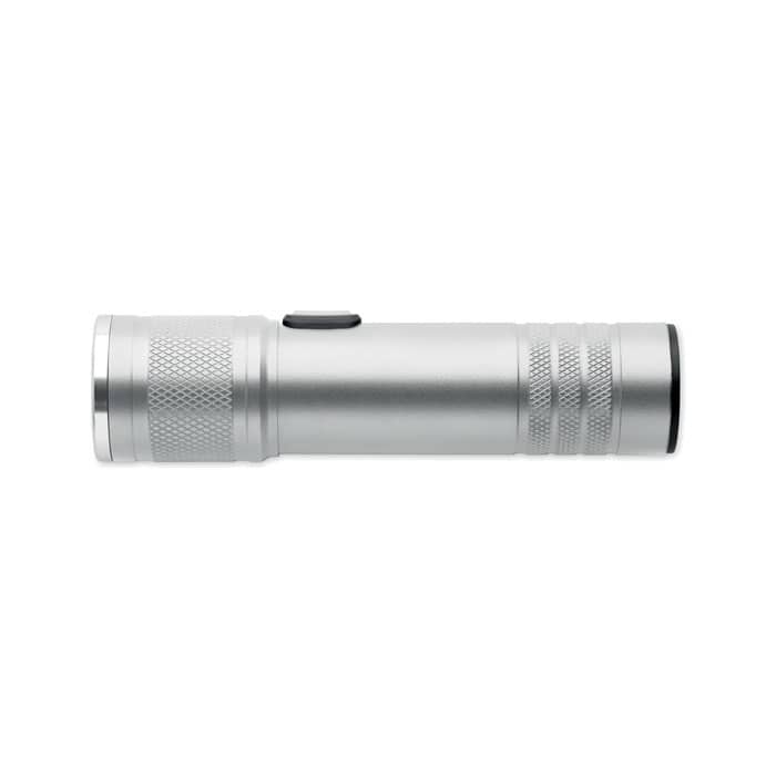 A silver flashlight with a textured grip and a black lens, featuring a side button for operation and a logo.