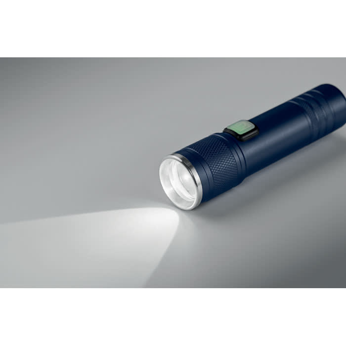 A blue flashlight is positioned on a grey surface, showcasing its shiny silver light beam and textured grip.
