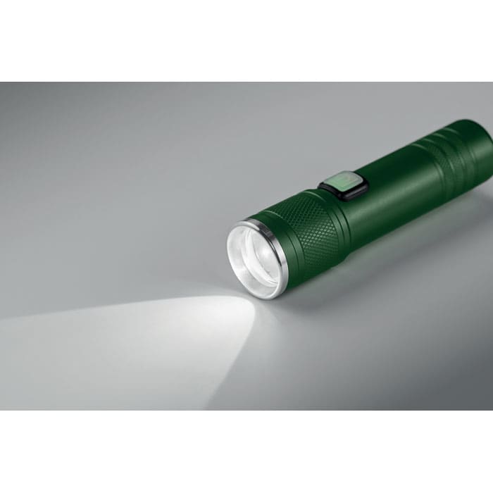 A green flashlight with a textured grip and a silver reflector, casting a beam of light. It features a power button.