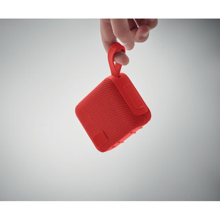 A red portable speaker with a textured surface and a handle is being held by a hand.