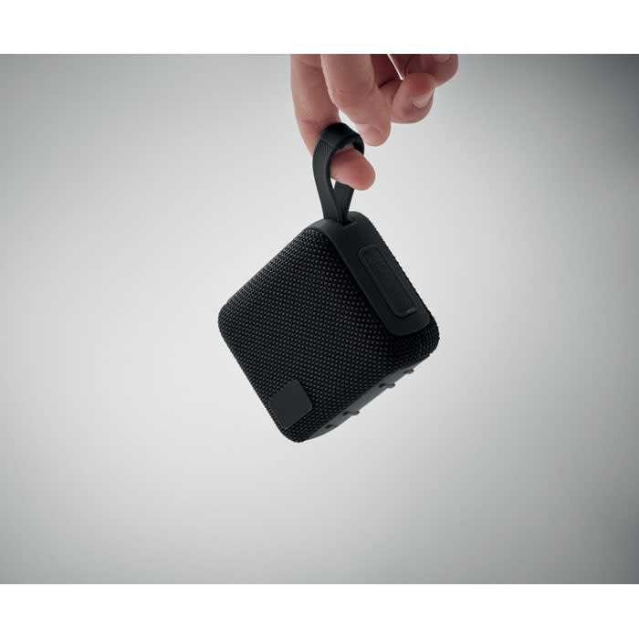 A portable black speaker is held by a loop attached to the top, showcasing its compact design.