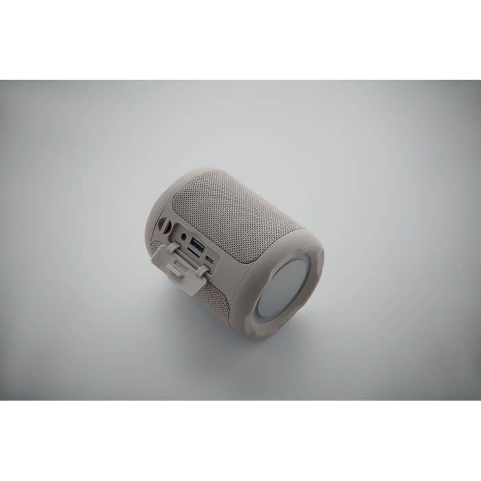 A portable speaker in a beige colour with a textured surface and a visible logo.