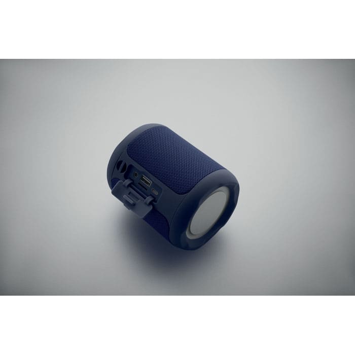 A cylindrical blue speaker with a textured surface and control buttons. It has a logo on its side.
