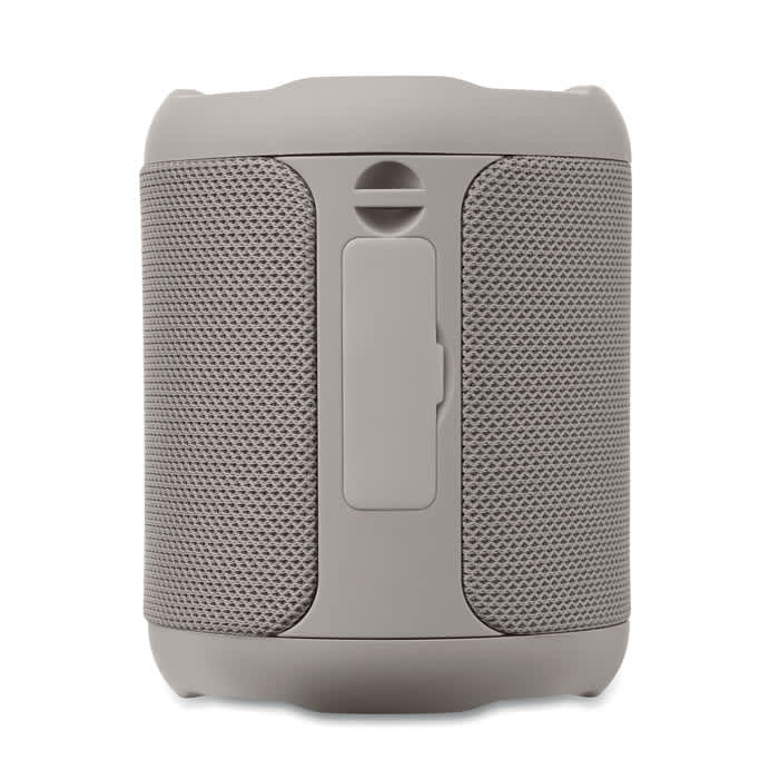 A grey portable speaker with a textured surface and a central control panel. It features a branding logo.