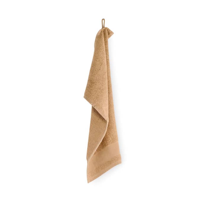 A tan towel hanging on a hook, showcasing its textured fabric and decorative hem.