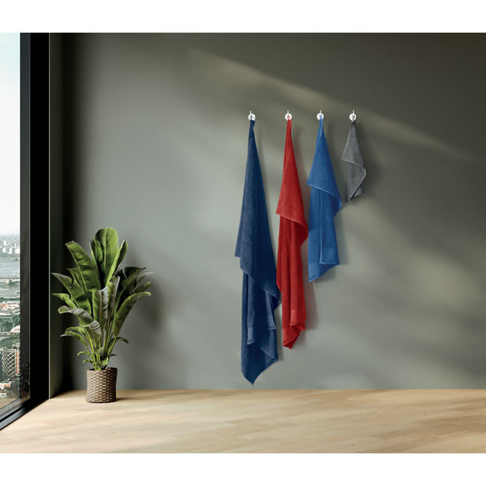 Three hanging towels in red, blue, and grey drape from hooks against a wall, with a potted plant nearby.