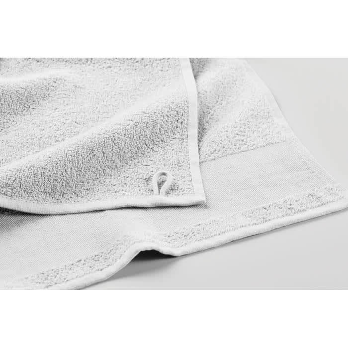 A white towel with a textured fabric, featuring a small logo on the edge.