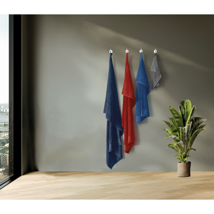 A collection of three hanging towels in red, blue, and grey, displayed against a neutral wall with a potted plant below.