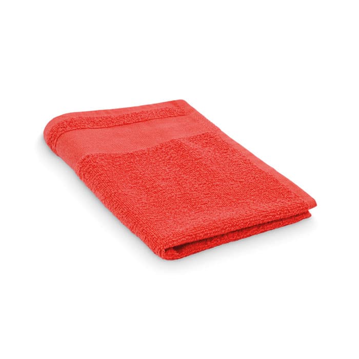 A red towel neatly folded, featuring a textured surface and a simple design. It has a small loop for hanging.