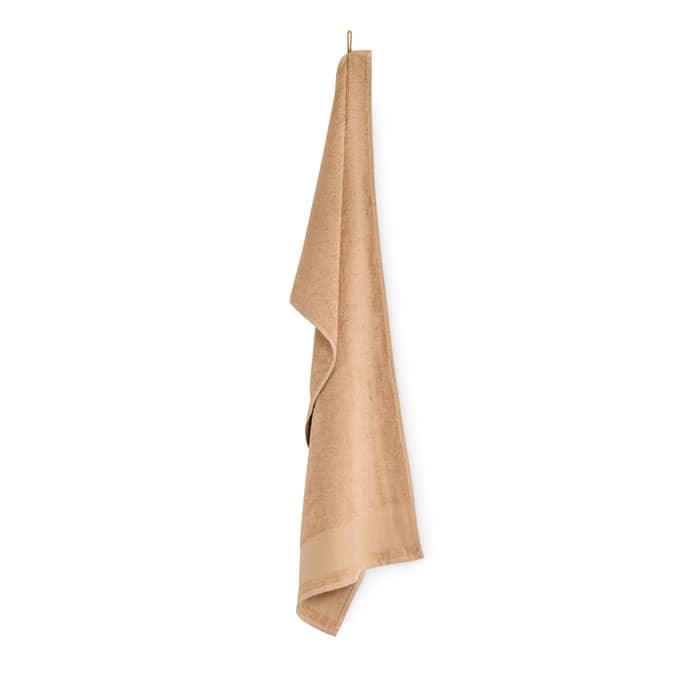 A towel in a soft, sandy beige hue is elegantly hanging, showcasing a smooth texture and a subtle sheen.