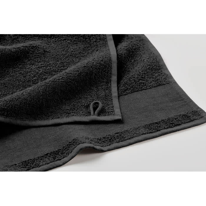 A black towel with a textured surface and a loop for hanging. The edges are neatly finished with a contrasting border.