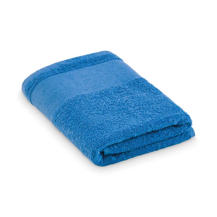 A blue towel, neatly folded, showcasing a textured design with a smooth band. It features a logo on one corner.