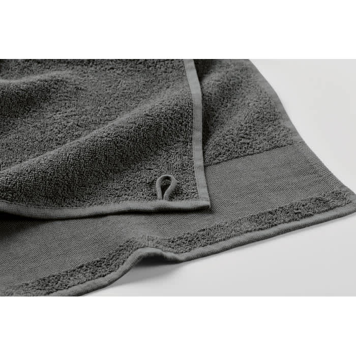 A grey towel with a textured design and stitched edges, featuring a small loop for hanging.