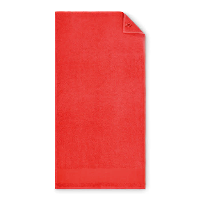 A red towel with a folded corner, featuring a small logo. Soft texture and vibrant colour.