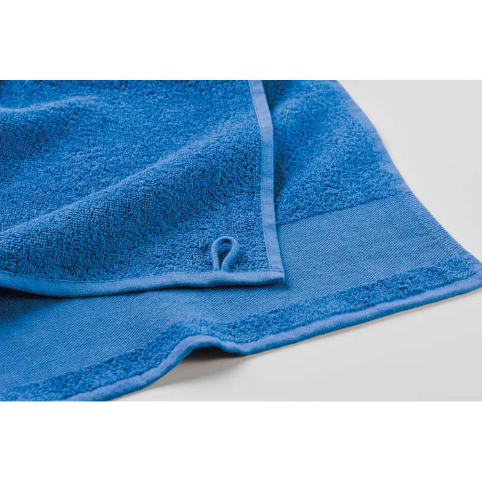 A blue towel with a textured surface and a contrasting border, featuring a small loop for hanging.