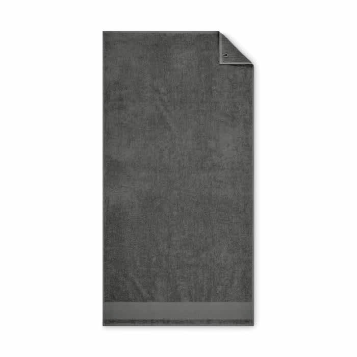 A dark grey towel with a textured surface and a folded corner, featuring a small branding logo.