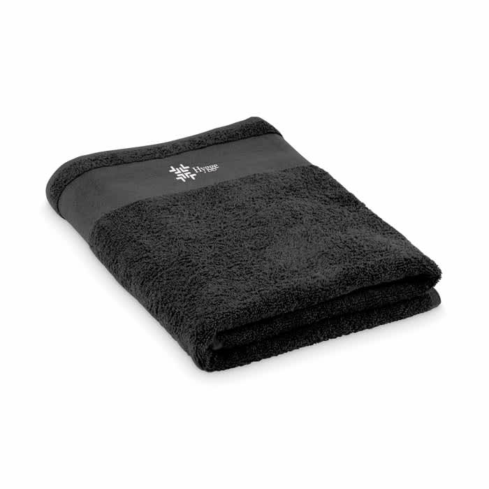 A folded black towel with a textured surface and a smooth black band at the top featuring a logo.
