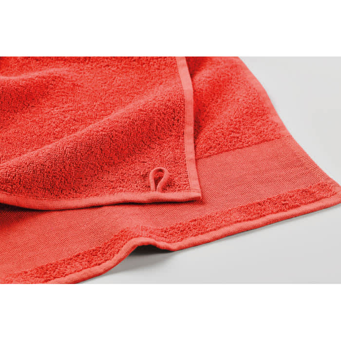 A terry towel in vibrant coral, featuring a hanging loop and textured surface.