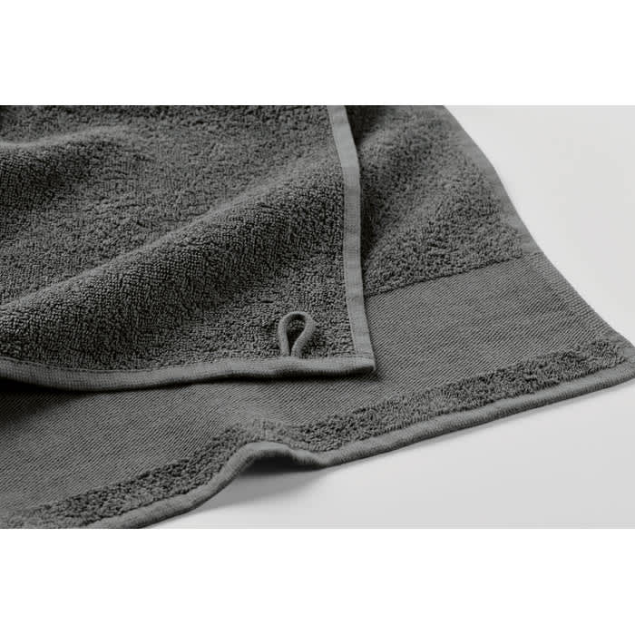 A grey towel laid flat, featuring a textured surface and a loop for hanging. The edges are neatly finished.